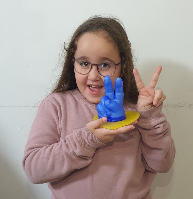 ילדה עם יד שעווה כחולה בתנוחת ניצחון